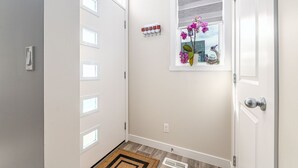 Un couloir propre et moderne, avec une porte blanche, une petite fenêtre donnant sur le ciel, un panneau d’accueil et une prise de courant.
