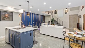 Une cuisine moderne avec un îlot central bleu, un coin repas doté d’une table en bois et un escalier menant à un niveau supérieur.