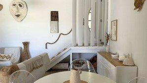 A modern, minimalist bedroom with a white color scheme, a staircase, and a dining area with a table and chairs.