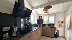 A modern kitchen with a black stove, wooden cabinets, and a large window overlooking greenery.