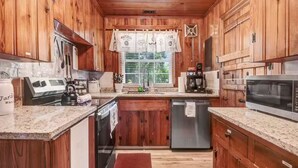A kitchen with wooden cabinets, granite countertops, a stainless steel refrigerator, a dishwasher, a coffee maker, and a microwave. - The Whimsical Barn (Rocky Mount)