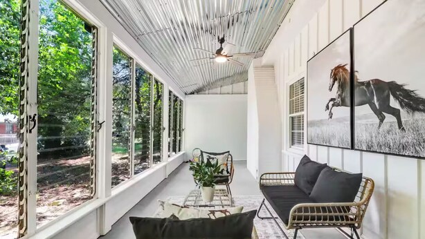 A room with large windows, a ceiling fan, a sofa, a chair, and a painting of a horse. - The Whimsical Barn (Rocky Mount)