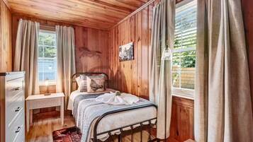A wooden-paneled room with a bed, a desk, and a window with curtains.