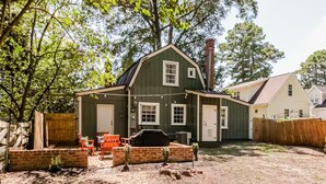 A two-story house with a green exterior, a brick patio, and a barbecue grill in front. - The Whimsical Barn (Rocky Mount)