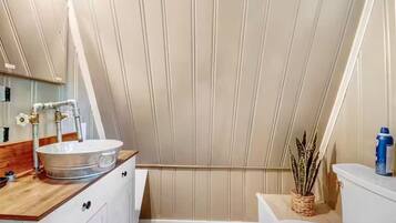 Un baño con tocador de madera, lavamanos blanco, espejo y retrete.