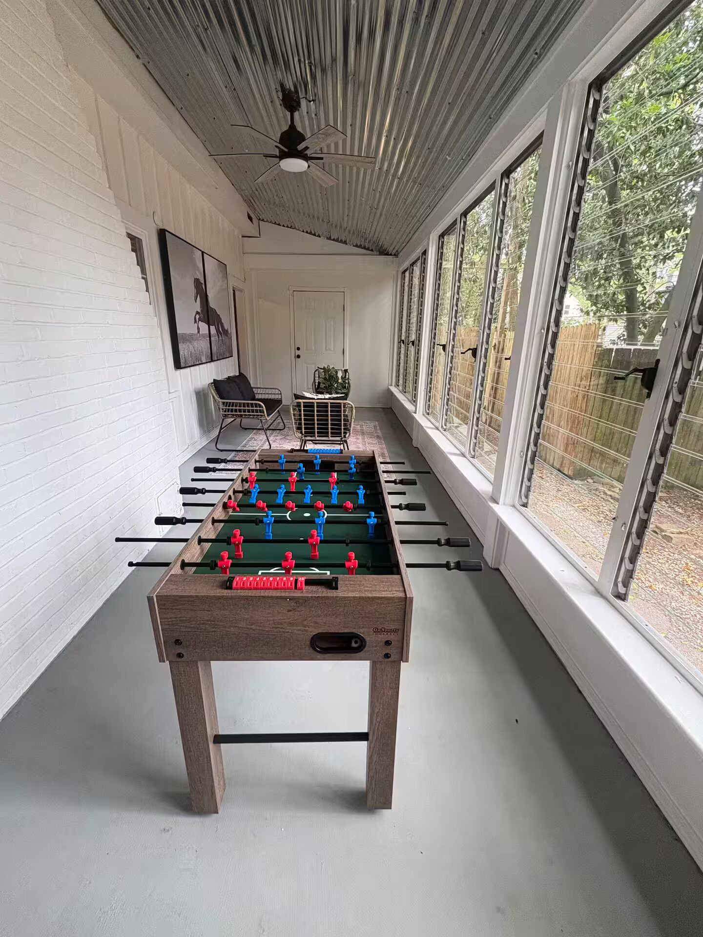 Une pièce avec une table de baby-foot, un ventilateur de plafond et de grandes fenêtres.