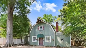 A rustic, single-story wooden house with a green door, white shutters, and a chimney. - The Whimsical Barn (Rocky Mount)