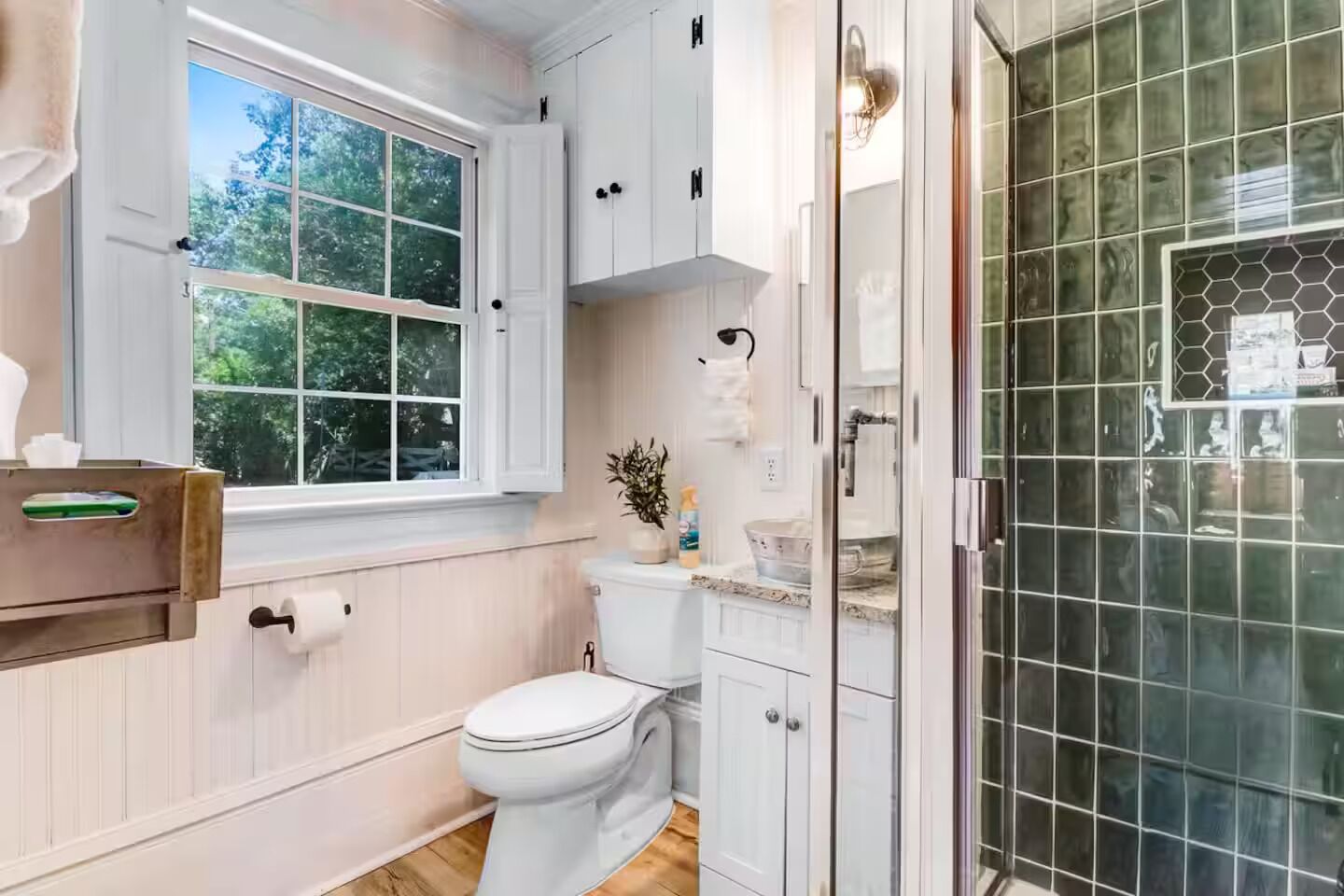 Een badkamer met toilet, een raam, kastjes en een douchehoek.