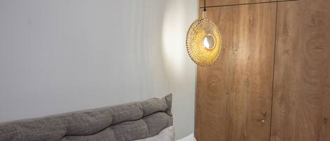 A bedroom with a wooden wardrobe, a bed with grey and white bedding, and a woven light fixture.