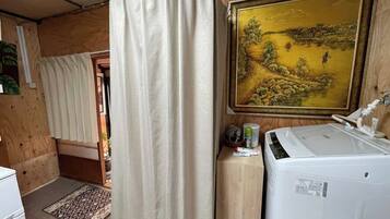 A compact room with a wooden interior, a washing machine, a painting on the wall, and a curtain.