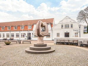 Uma praça de paralelepípedos com uma escultura de pedra, bancos e um edifício com telhado de azulejos.