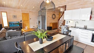 A modern interior with a wooden ceiling, a dining area with a black table, a sofa, and a kitchen with white cabinets.
