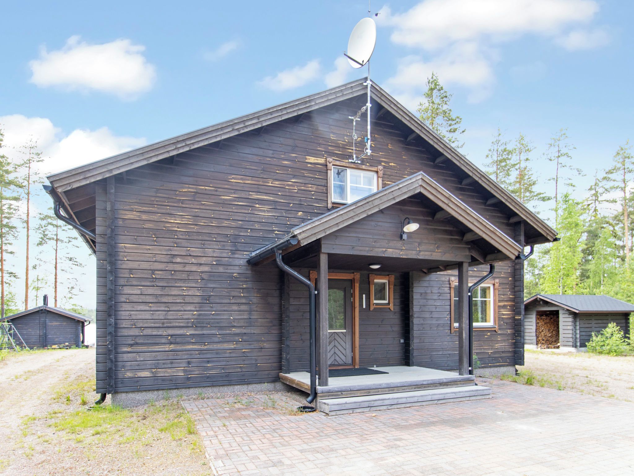 A wooden cabin with a satellite dish, a porch, and a small attached shed.