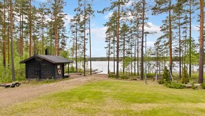 Une cabane avec un quai, entourée de grands pins et bordant un lac.