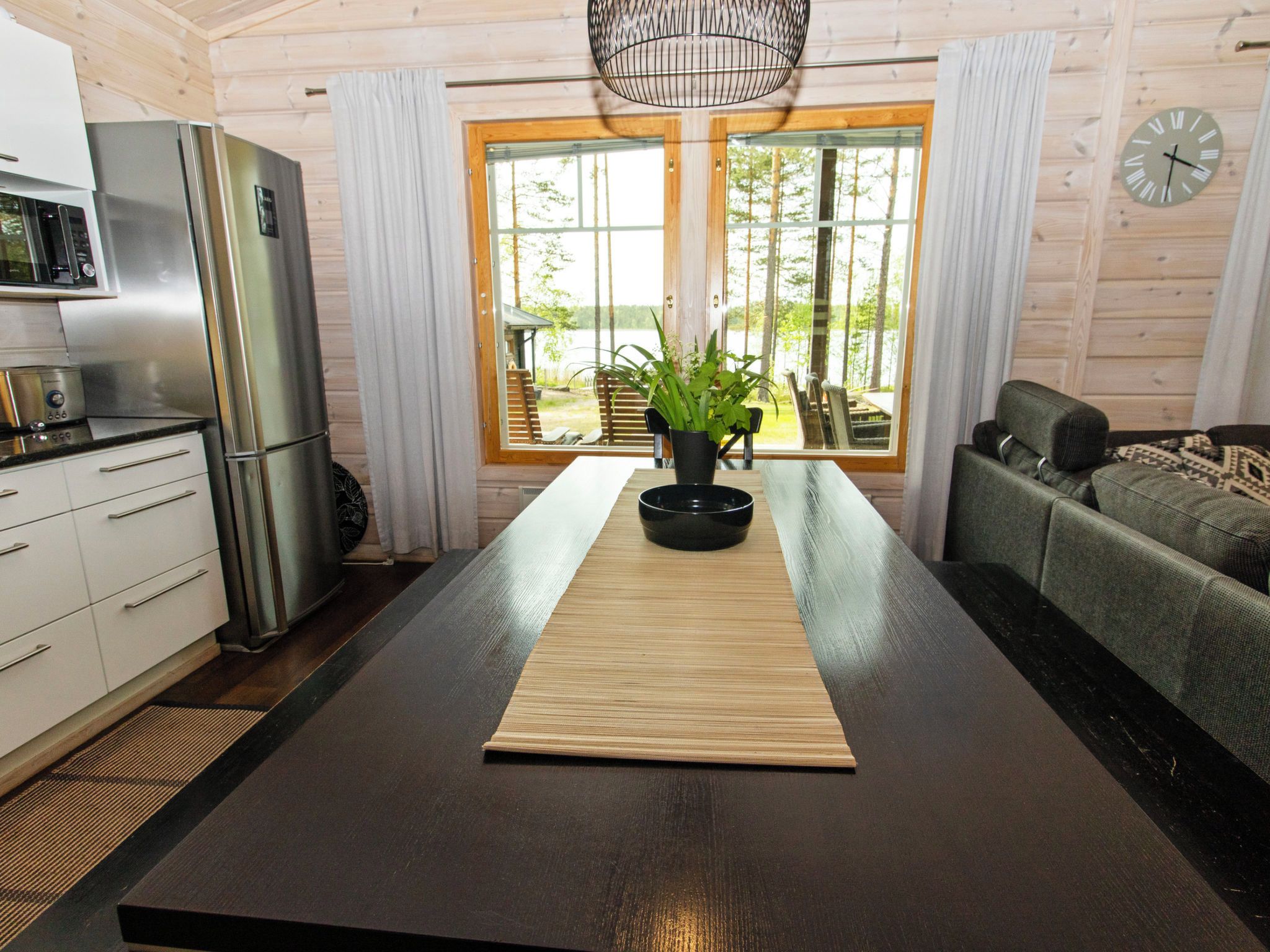 A modern kitchen with a central island, a refrigerator, and a dining area with a view of the outdoors.