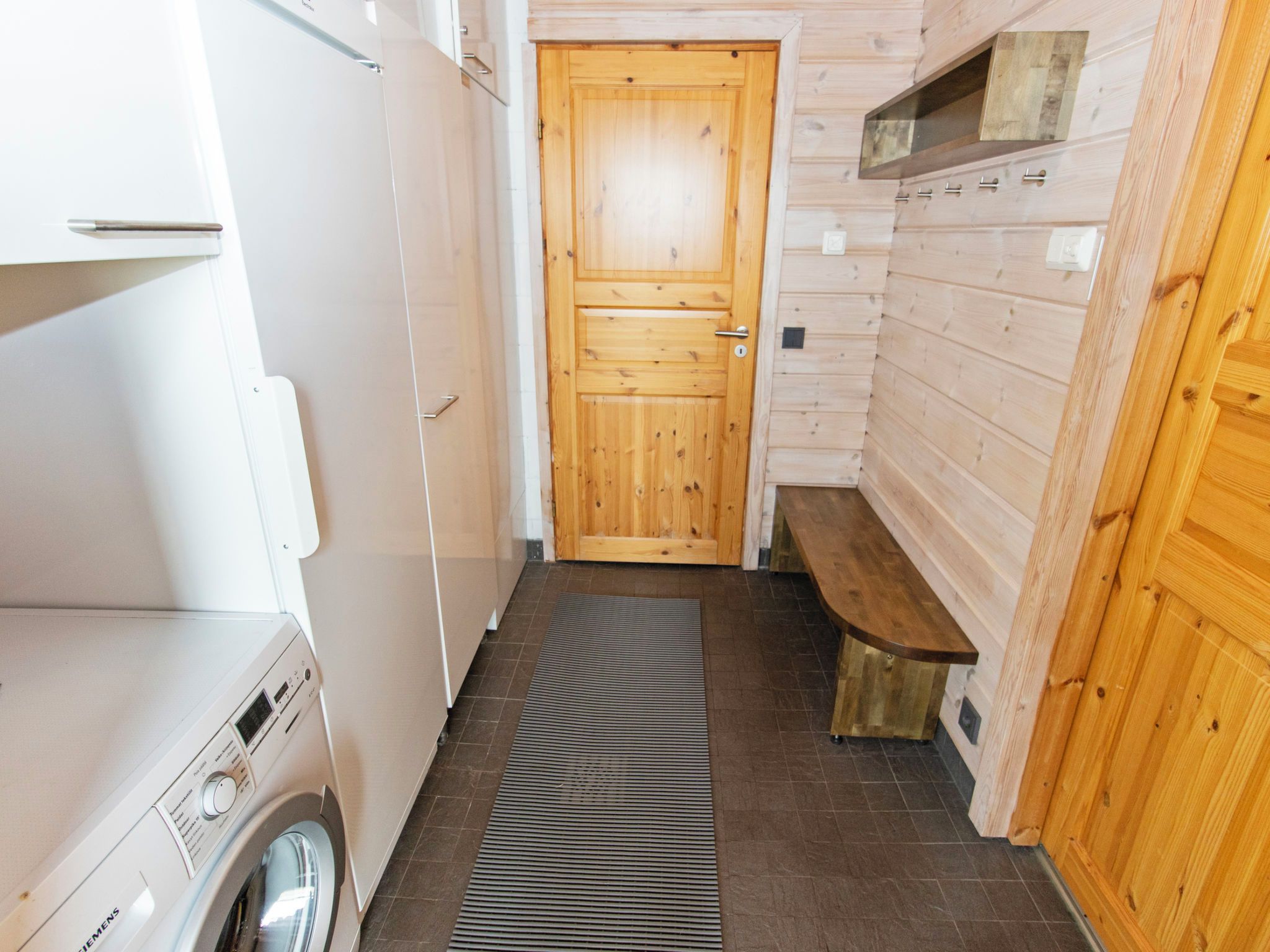 A compact bathroom with a wooden door, a bench, and a washing machine.