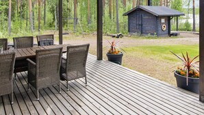 Une terrasse en bois, agrémentée de meubles en osier et de plantes en pot, qui offre une vue sur une forêt et un petit chalet.