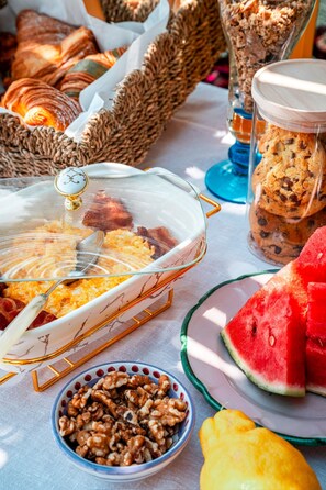 Een buffet met diverse gerechten, waaronder een ovenschotel, koekjes, walnoten en stukken watermeloen.