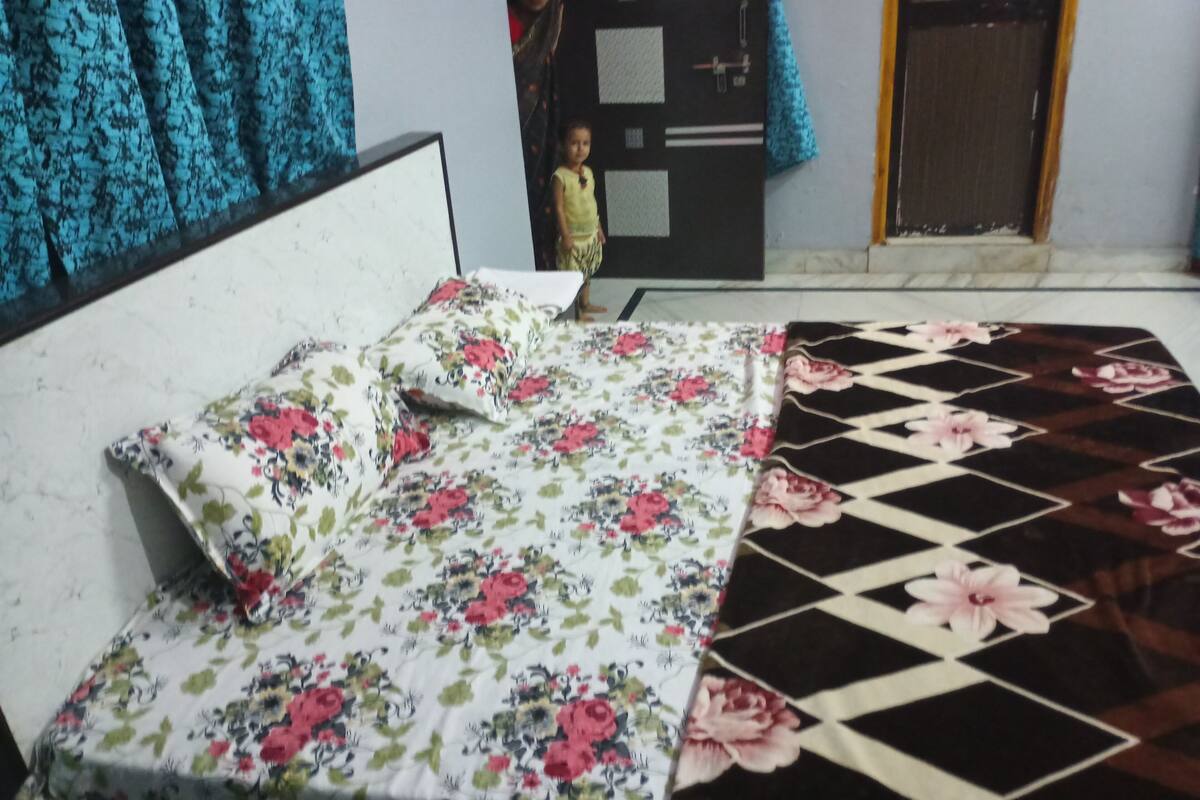 A bed with floral and geometric patterned bedspreads, a white headboard, and a blue curtain in the background.