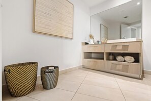 Un baño con un espejo grande, un tocador de madera y dos cestas tejidas.