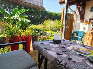 A wooden deck with a table covered in a patterned tablecloth, surrounded by potted plants and a wooden fence.
