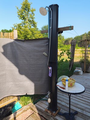 Eine Außendusche mit Schlauch, Handtuchhalter und einem Tisch mit Toilettenartikeln.