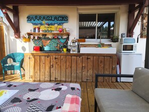 Een houten terras met een keukenhoek, een eettafel en een stoel.