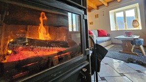 Un salon chaleureux avec un poêle à bois, un canapé, une fenêtre avec des rideaux et un ventilateur de plafond.
