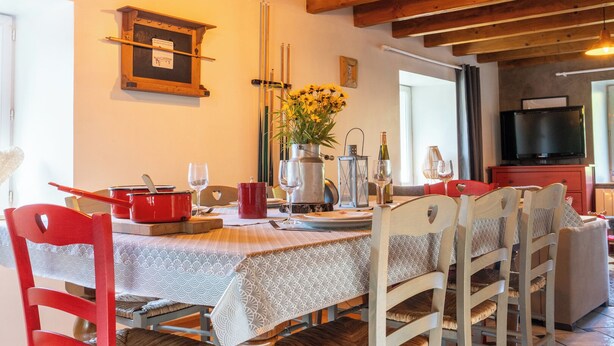 Un coin repas avec une table en bois dressée pour deux personnes, une nappe à motifs rouges et blancs, et un vase rempli de fleurs jaunes.