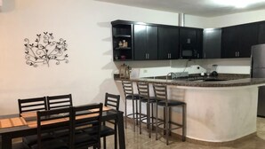 Una cocina moderna con armarios oscuros, encimera de granito y una isla central con taburetes de bar.