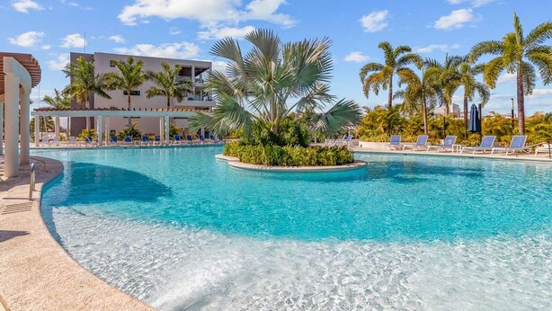 A swimming pool with lounge chairs and palm trees, surrounded by a building with a modern design.