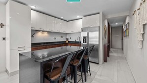 A modern kitchen with white cabinets, a stainless steel island, and bar stools.
