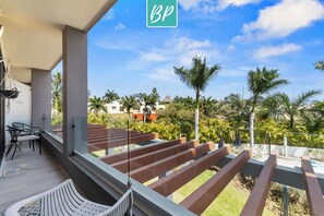 A balcony with a view of palm trees and buildings, a chair, and a table. - Quadrant 206: Pool, Gym & Padel – Walk to Beach! (Bucerías)