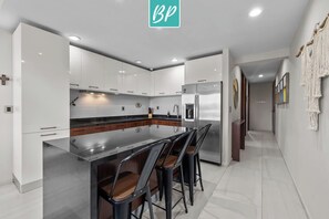 Una cocina moderna con armarios blancos, una isla de acero inoxidable y taburetes de bar.