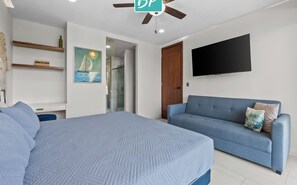 Un dormitorio con una cama, un sofá azul, un televisor montado en la pared y un ventilador de techo.