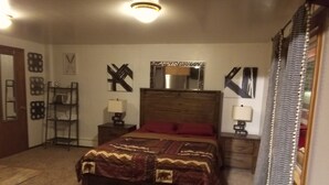A bedroom with a large bed, two bedside tables, a nightstand, a wall-mounted mirror, and a shelf with decorative items. - Charming 1-bedroom unit in gorgeous Custer with WiFi car rental available. Suite (Custer)