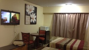 Una habitación de hotel con dos camas, un escritorio, una silla, un televisor y un microondas.