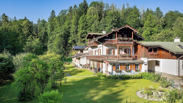 Een ruime houten chalet met meerdere balkons, omgeven door weelderige begroeiing en een verzorgd gazon.