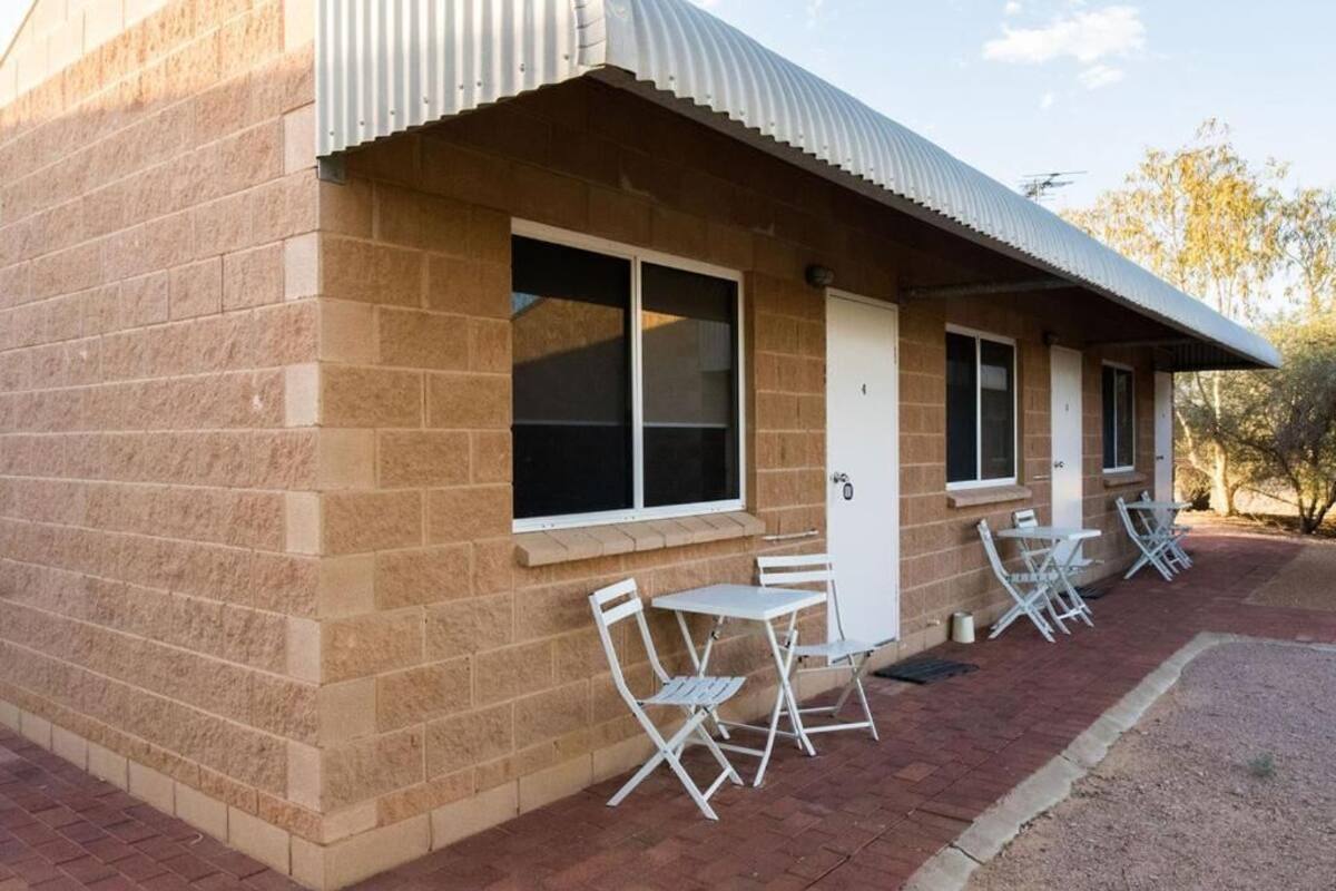 A building with a brick exterior, a corrugated metal roof, and a patio area with white metal chairs and tables.