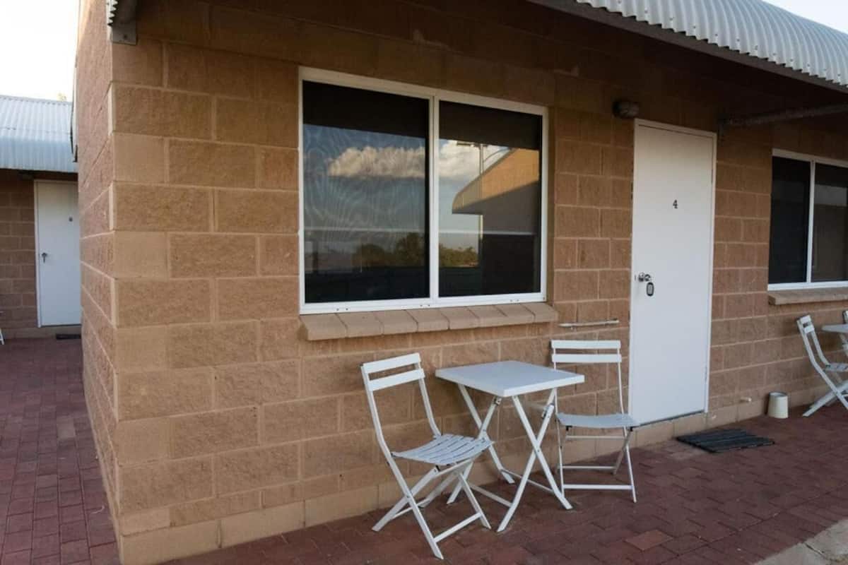 A brick building with a white door and window, two white folding chairs, and a small table.