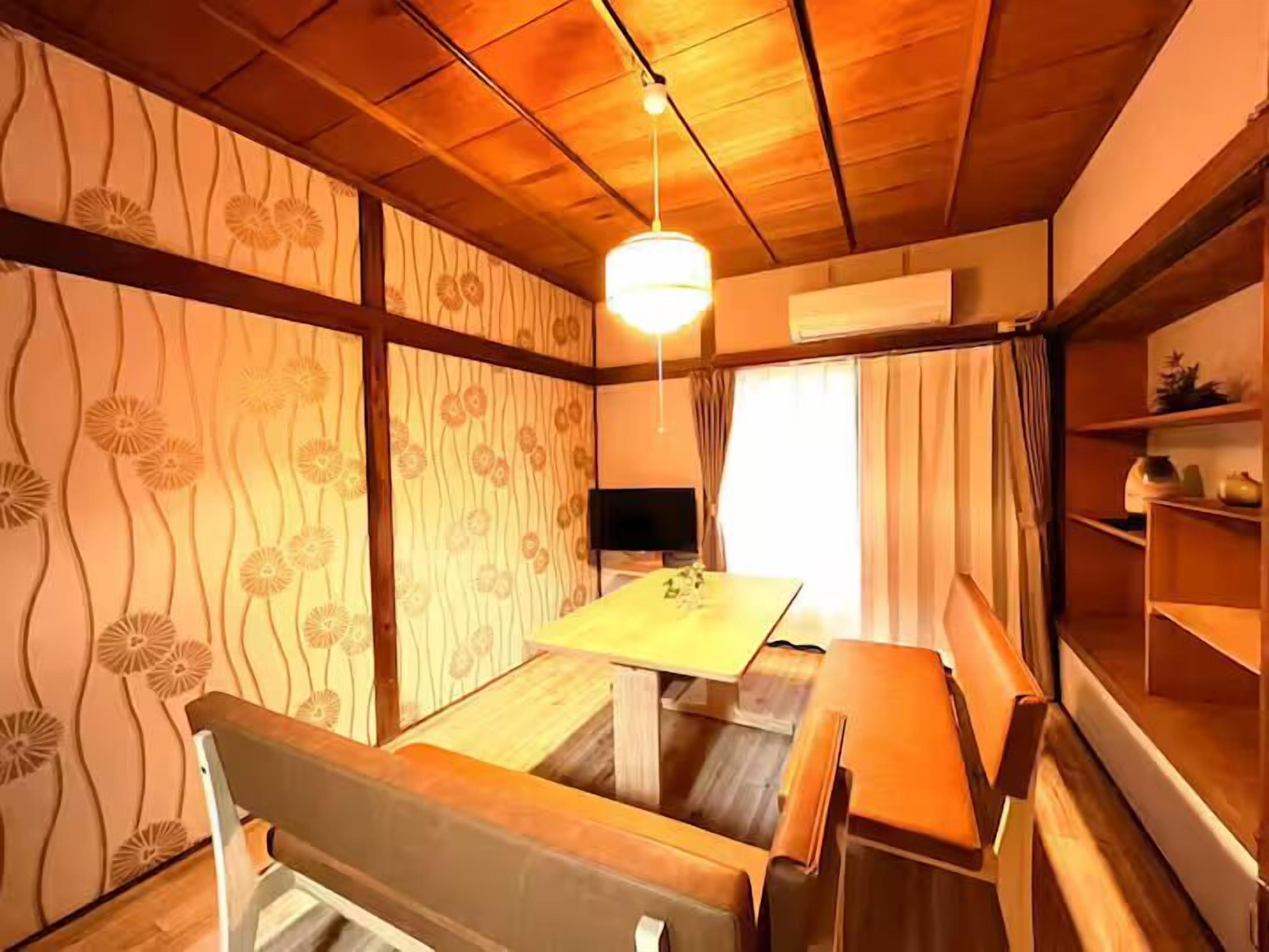 Een kamer met een houten plafond, een tafel, stoelen, een televisie en een plank met decoratieve objecten.