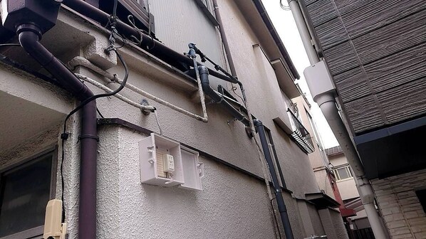 A building exterior with visible plumbing and electrical conduits, a window, and a door. - Akabanenishi Kodate (Tokyo)