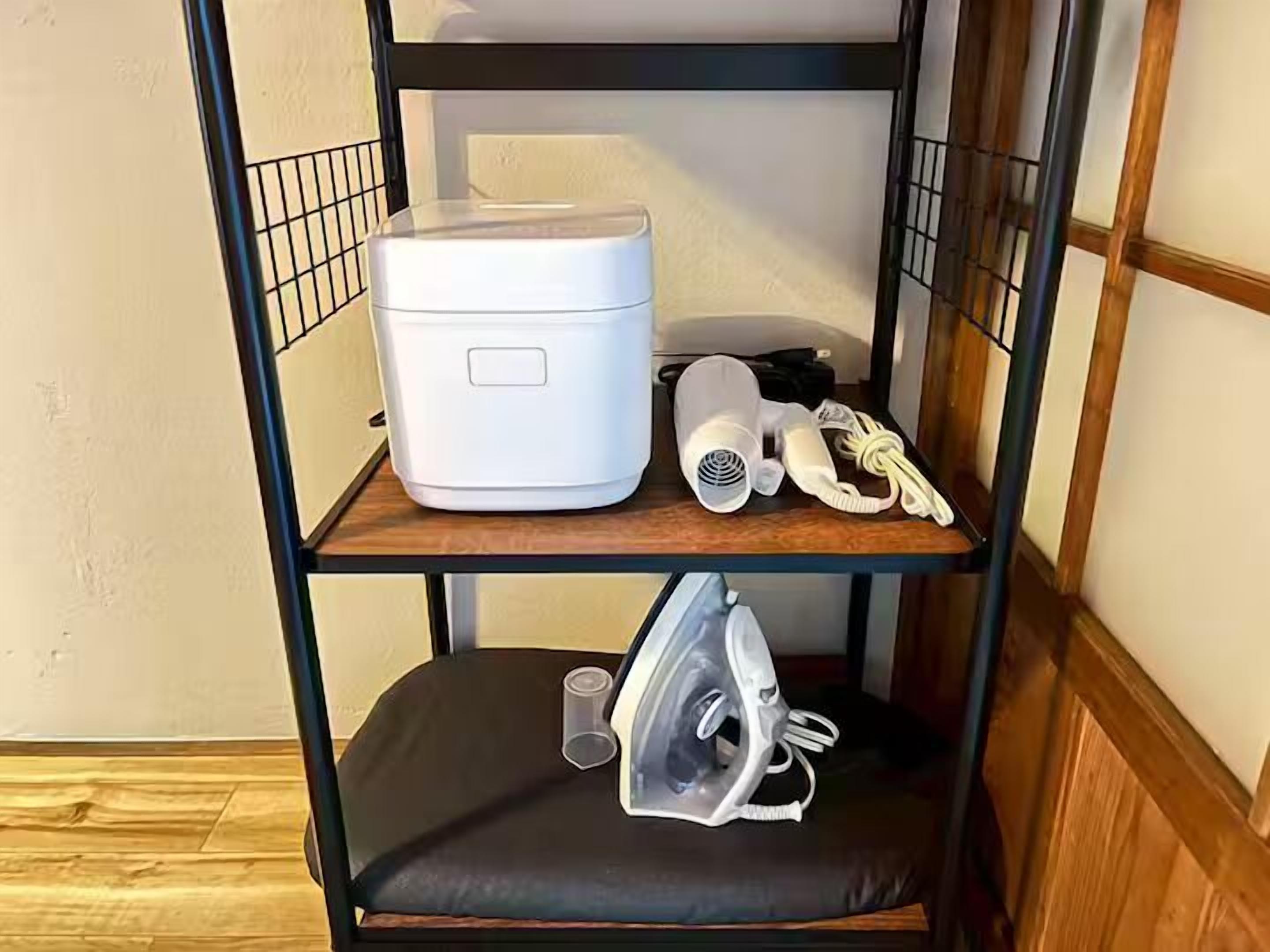 A bunk bed with a white appliance on the top shelf, a hairdryer and other items on the middle shelf, and an iron on the bottom shelf.