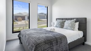 Une chambre avec un grand lit, deux fenêtres et une vue sur des maisons.
