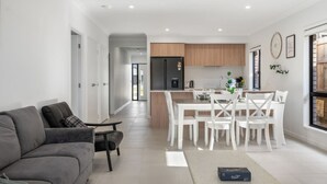 Un appartement moderne avec un canapé gris, un coin repas avec des chaises blanches, une cuisine avec des meubles en bois et une grande fenêtre.