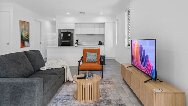Ein modernes Wohnzimmer mit einem grauen Sofa, einem orangefarbenen Sessel, einem Holztisch und einem Flachbildfernseher auf einem Holzboden.