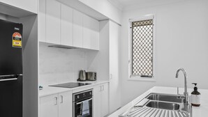 Eine moderne Küche mit weißen Schränken, einem schwarzen Kühlschrank, einer Edelstahlspüle und einem Fenster mit Gitterrost.
