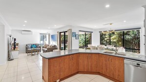 A modern kitchen with a curved island, large windows, and a dining area with outdoor seating. - Peaceful 4BR Retreat in Leafy Forest Lake Setting (Forest Lake)