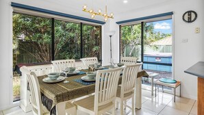 A dining area with a table set for six, white chairs, and a view of greenery outside. - Peaceful 4BR Retreat in Leafy Forest Lake Setting (Forest Lake)