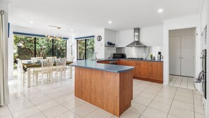 A modern kitchen with a central island, a dining area with a table and chairs, and a view of greenery outside. - Peaceful 4BR Retreat in Leafy Forest Lake Setting (Forest Lake)